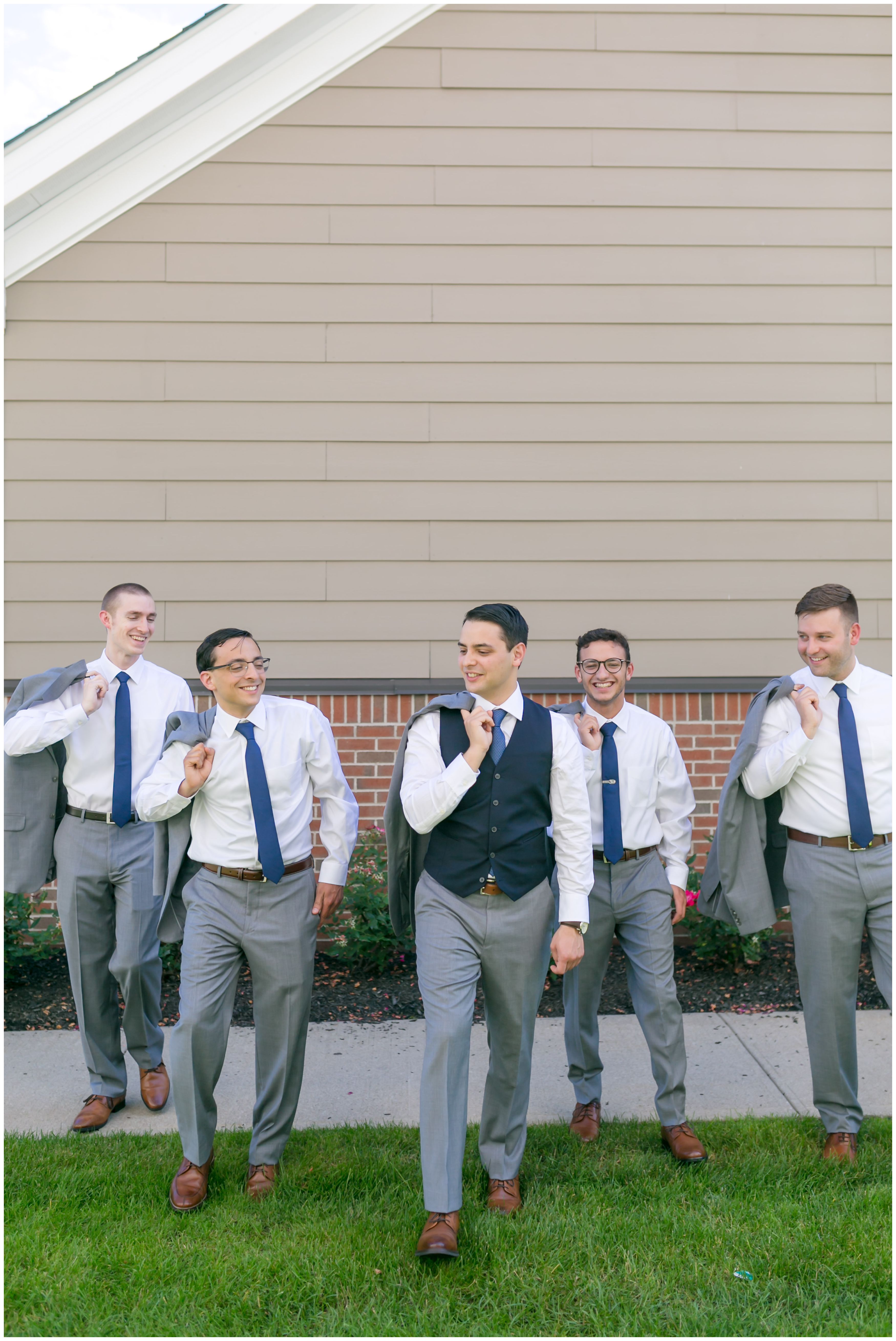 Groom and groomsmen in light grey suits and navy vests and ties with jackets off