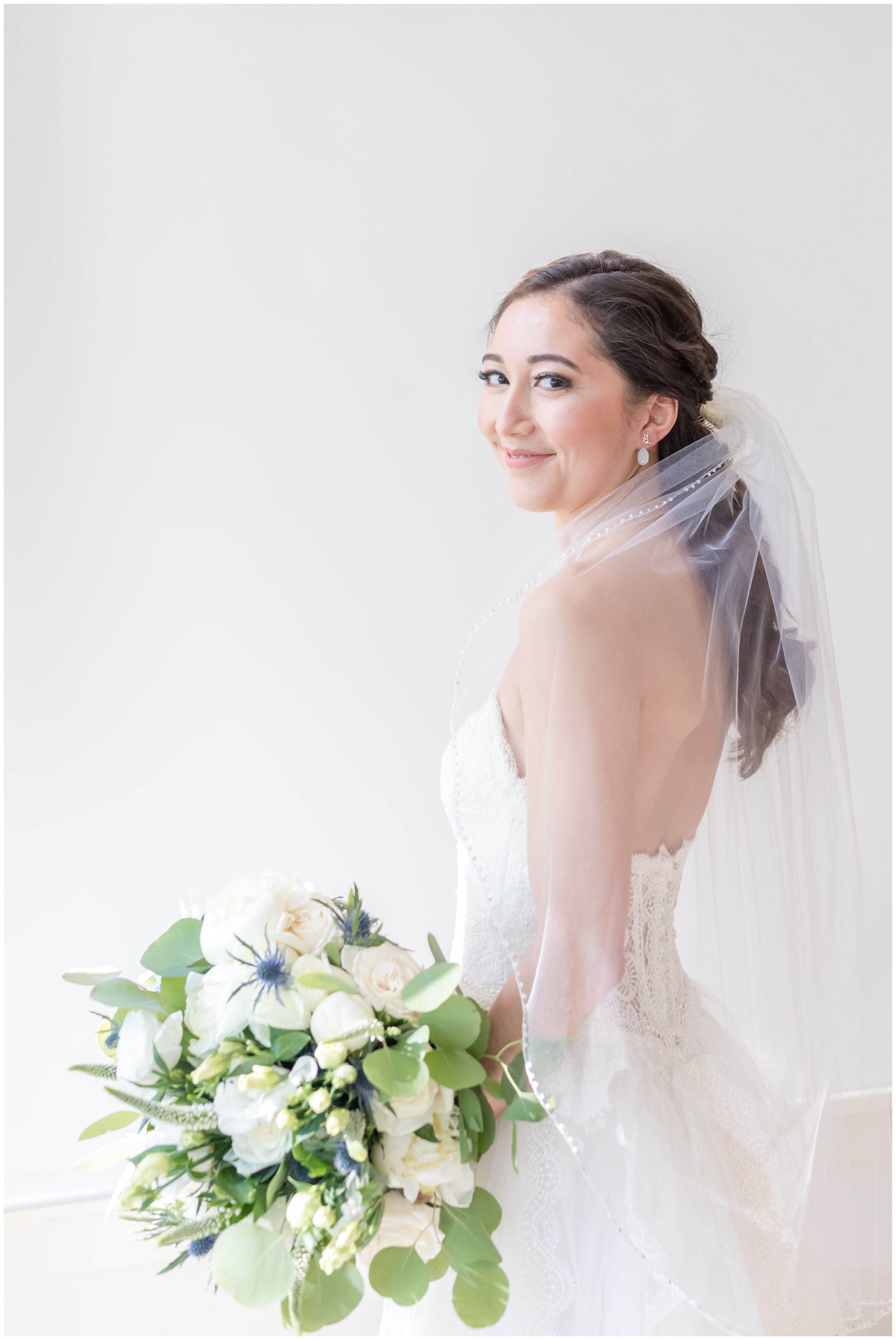 Bridal portrait with white peonies and roses bridal bouquet in strapless wedding white ballgown and veil