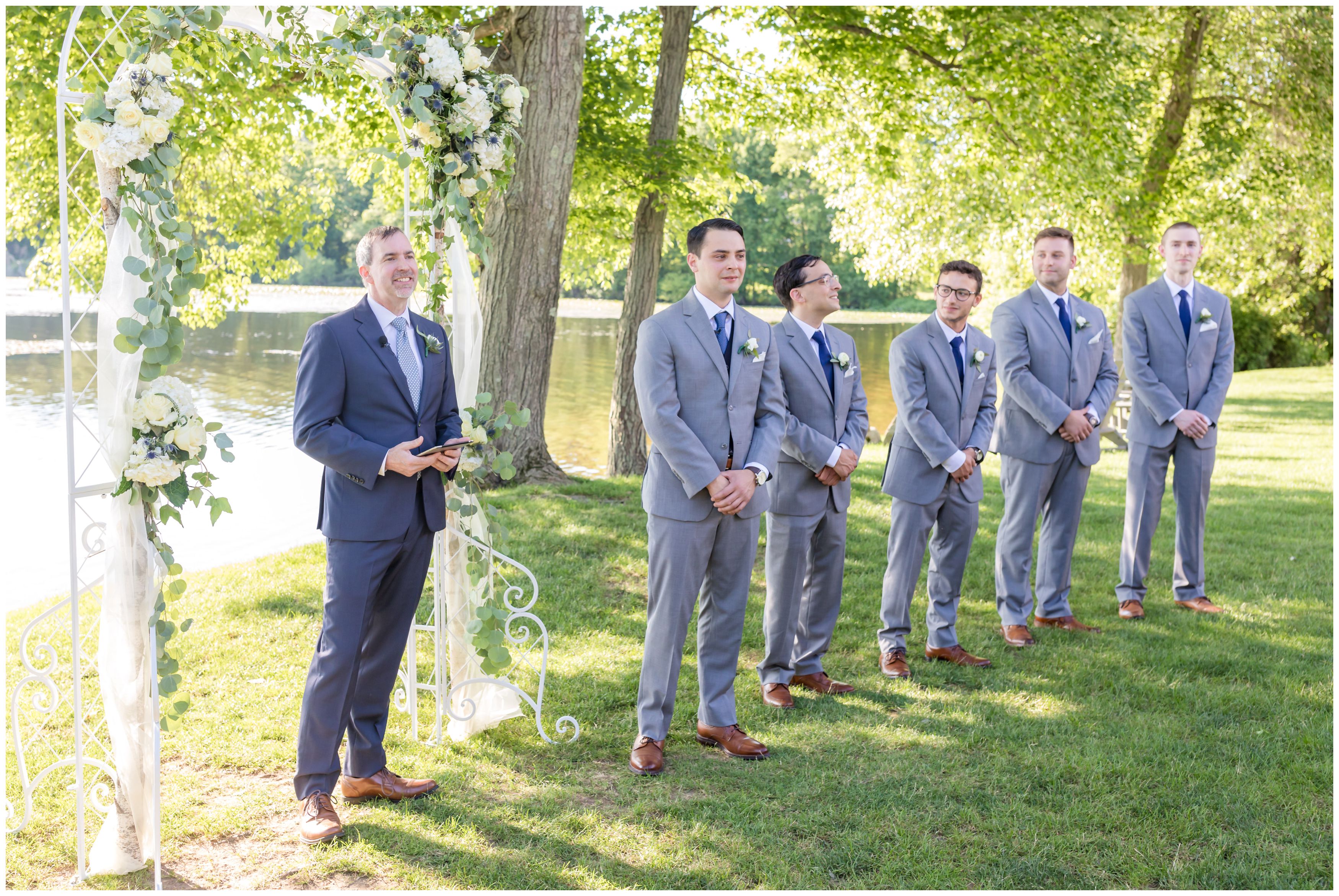 Officiant, groom and groomsmen at outdoor lakeside ceremony